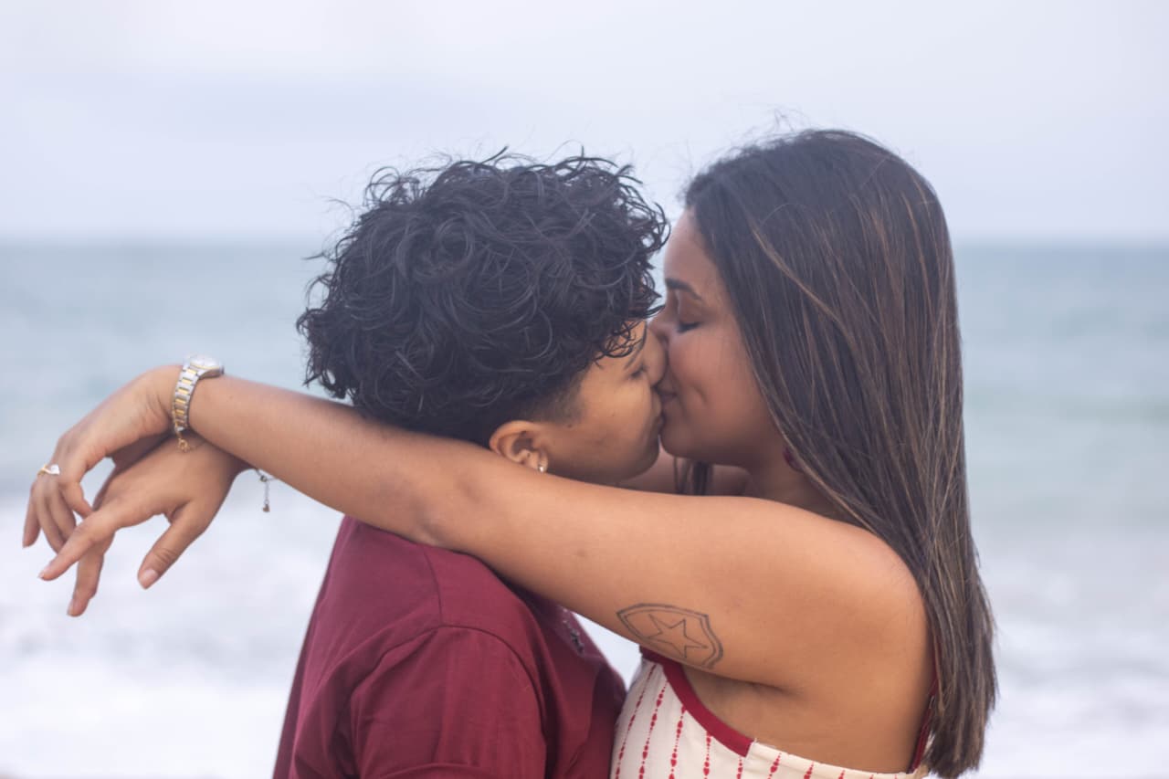 Casal se beijando na praia, ondas ao fundo